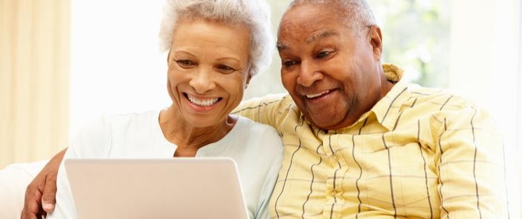 two older people smiling while looking at a laptop screen