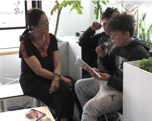 A boy speaks into a microphone as two others watch and listen