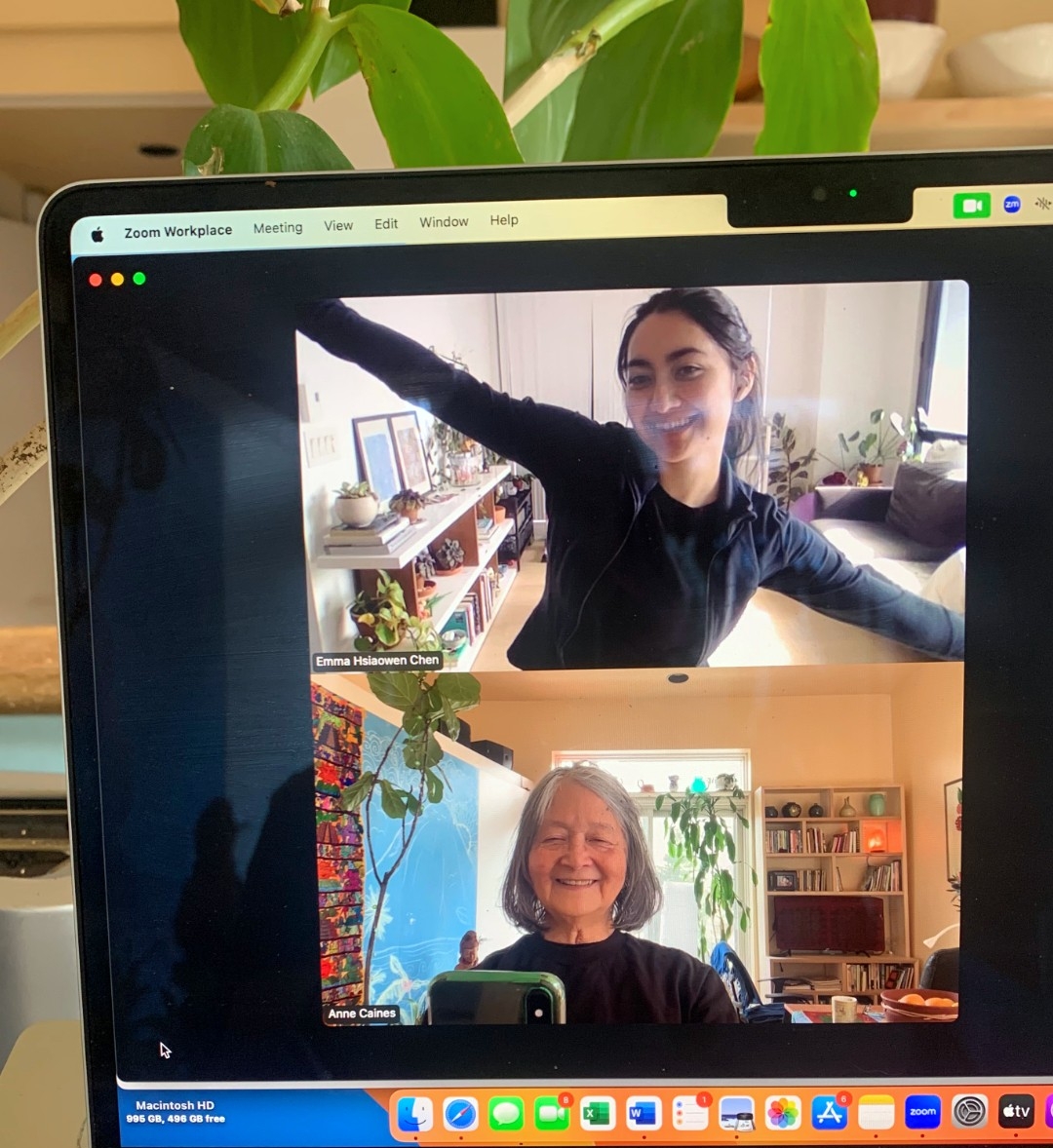 Photo of a laptop screen with a Zoom session open. Two Zoom squares are visible, on top, Emma smiles at the camera and has her arms outstretched. The bottom square has an older woman who is smiling and looking at her phone which is taking a photo of the screen.