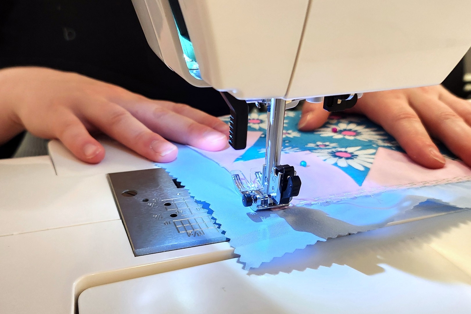 A person delicately feeds their quilted square through a sewing machine.