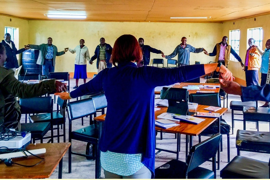 Un grand cercle de personnes se tenant par la main dans une salle remplie de chaises et de tables.