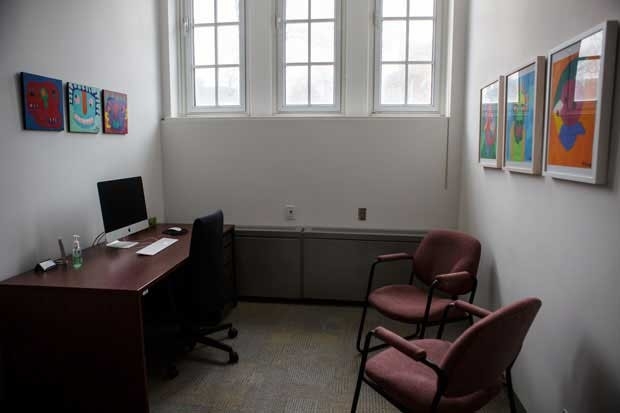 The individual research room is lit up by natrual light through the tall windows, showing the large desk and desk chair, the 5 paintings on the wall, and 2 red seats