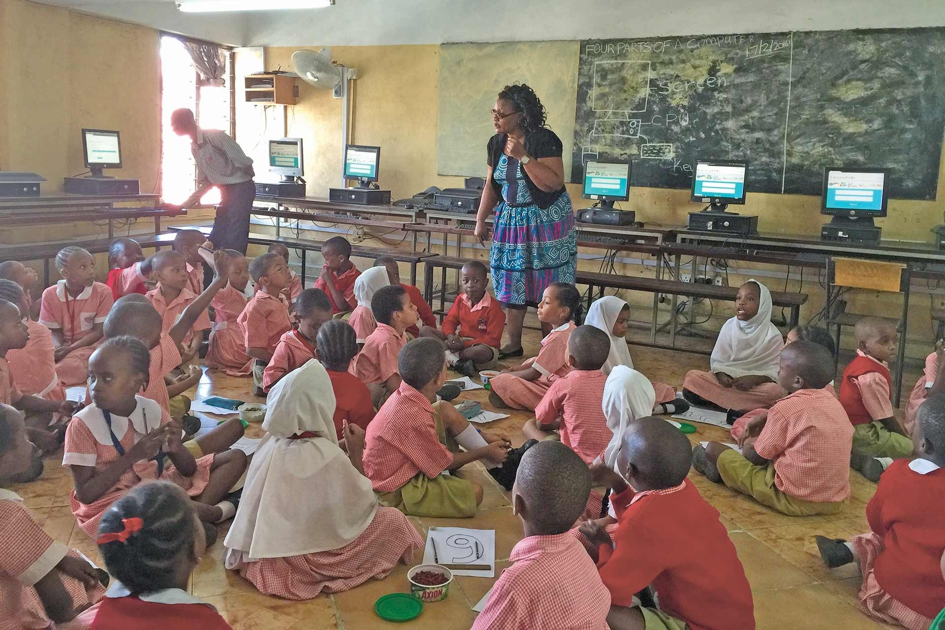 Classroom of children sitting on the floor in front of a teacher