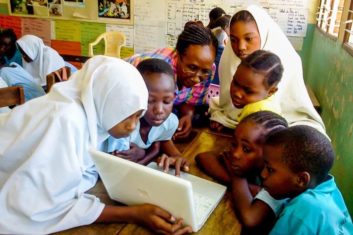 Children and their teacher, Joyce, huddle around a laptop