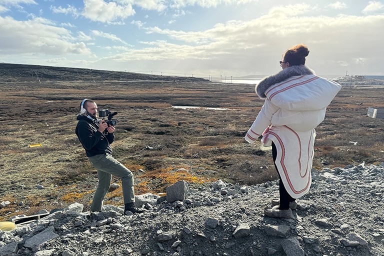 Concordia journalism research associate Luca Caruso-Moro photographs Aleashia Echalook, manager of Ajurisarvik and mother of three, outside her home in Inukjuak. Her three-month-old baby Dolly is nestled inside her amauti, a traditional parka worn by Inuit women. | Photo by Aphrodite Salas