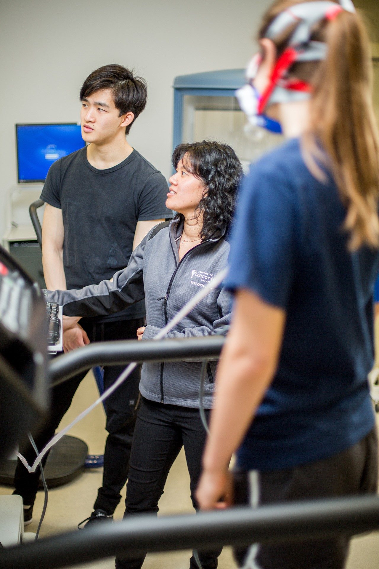 Become a research participant A person on a treadmill and two researchers examining data from a VO2 max test