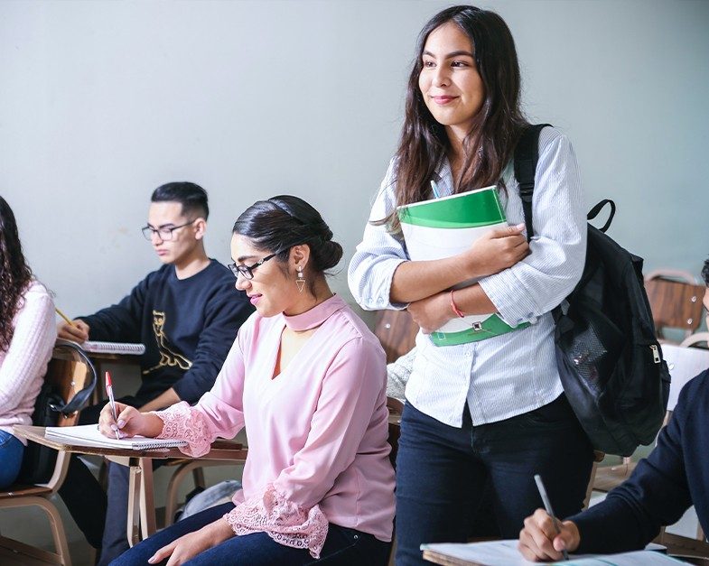 Student standing in class with books in hand