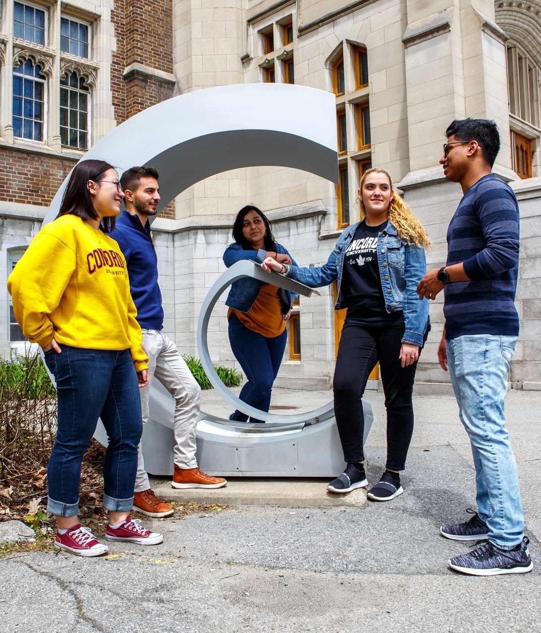 A group of students in conversation by a statue on Concordia University's Loyola Campus