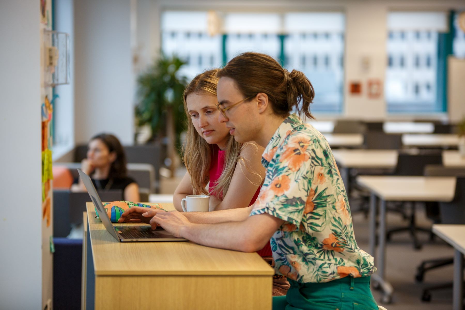 Young people in bright room look at laptop.
