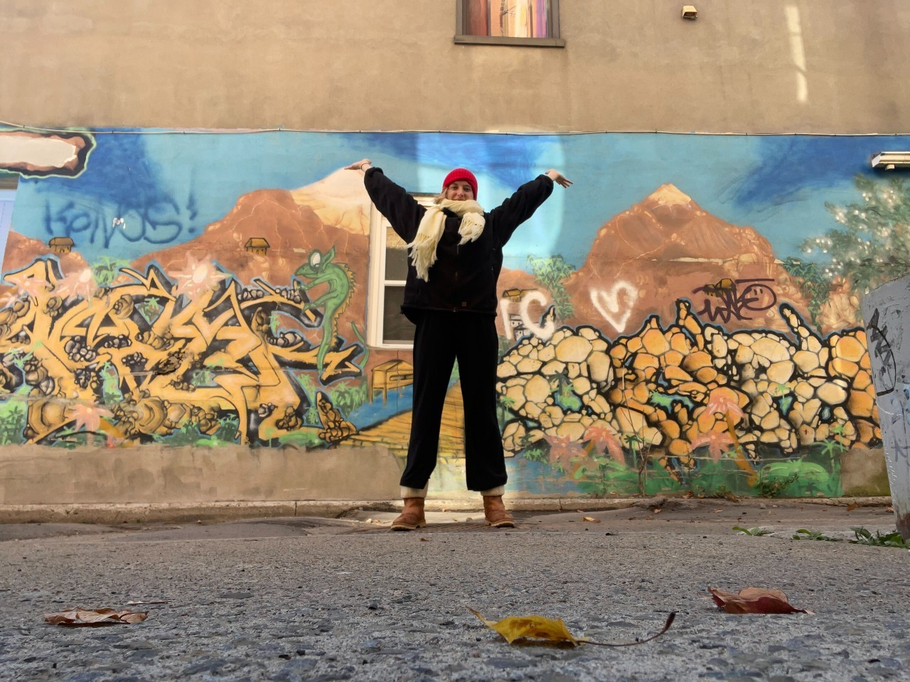 Amidst a November cold day, Jules mentor stands in front of Montreal street art with winter gear and her hands up. 