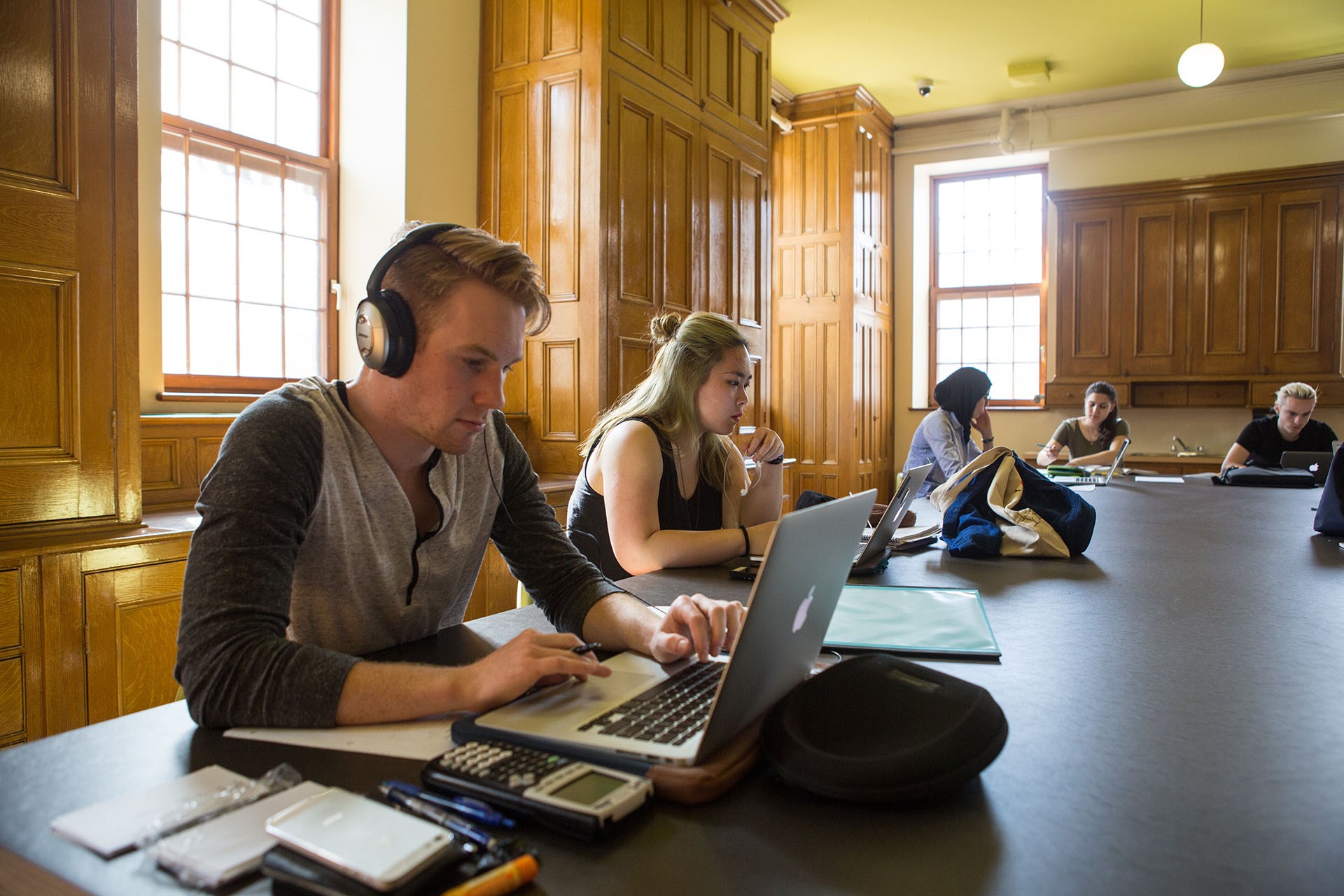 Students study at a large table in a brightly lit room with ornate wooden walls.