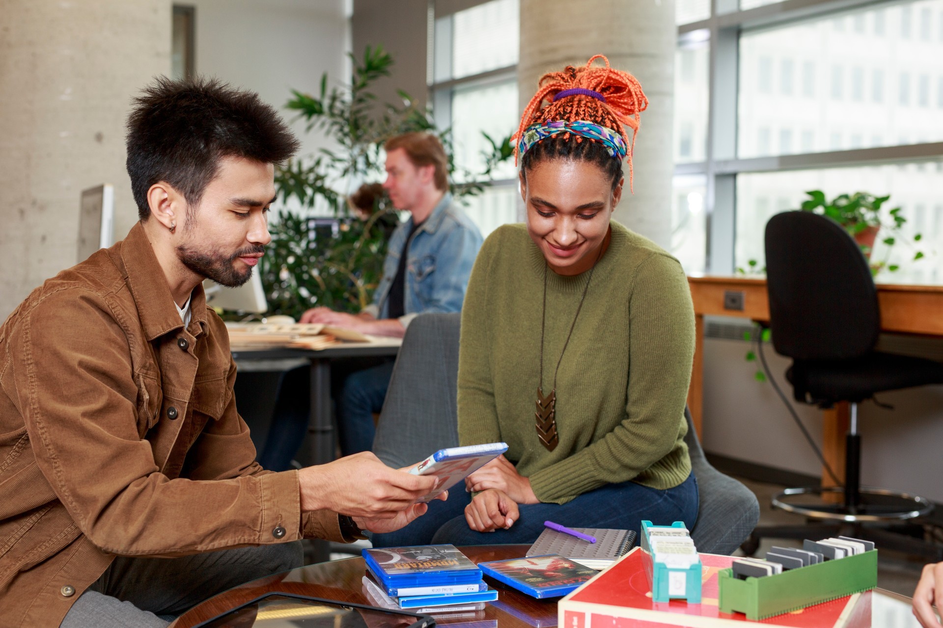 A man and a woman sort through DVDs while another man sits at a computer in the background. A man and a woman sort through DVDs while another man sits at a computer in the background.