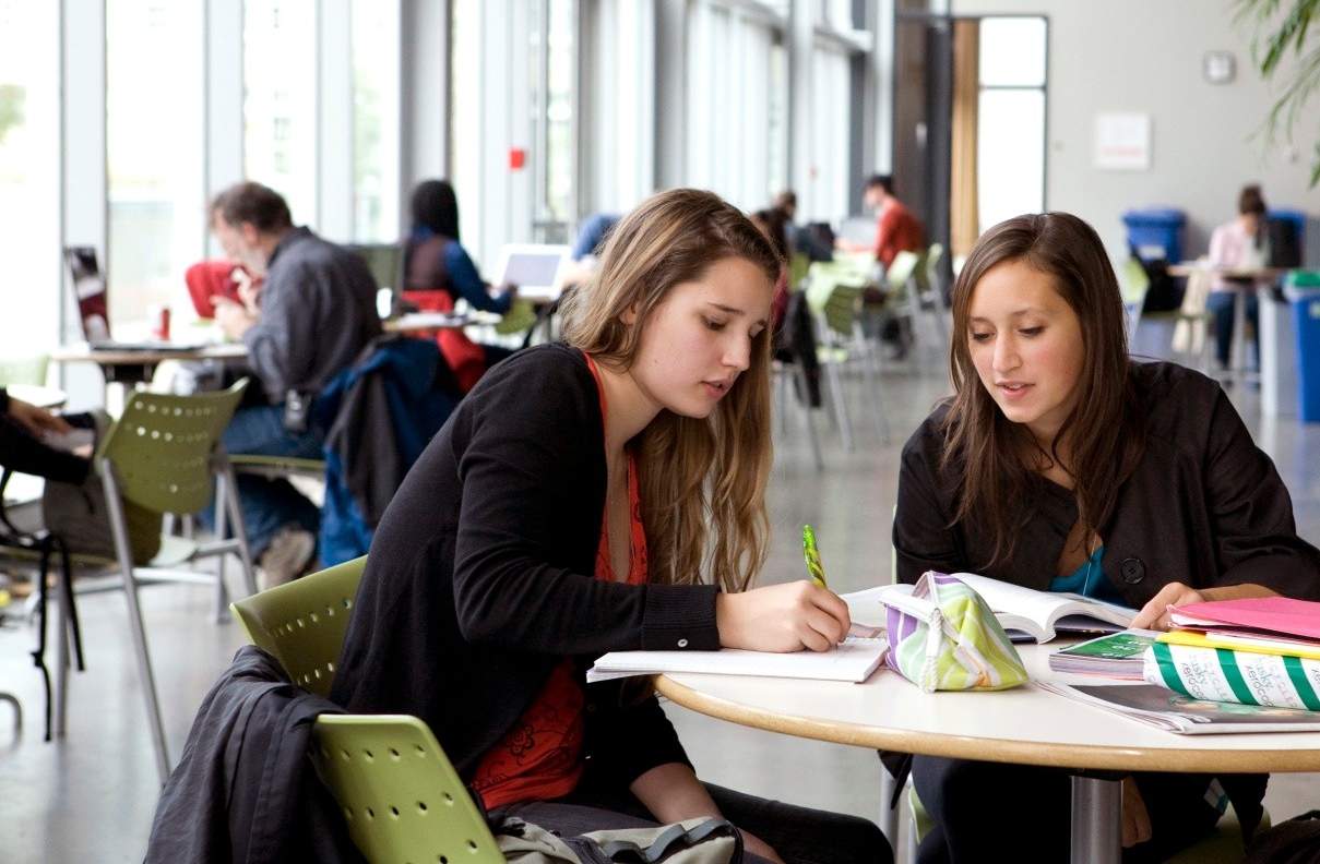 Two girls study at a table in a large, brightly lit atrium.