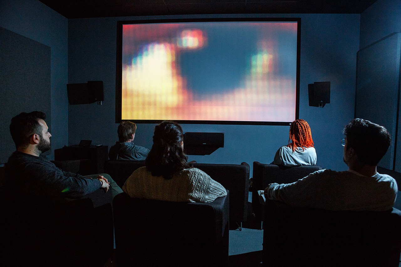 A room with comfortable looking bucket chairs that face a large screen.