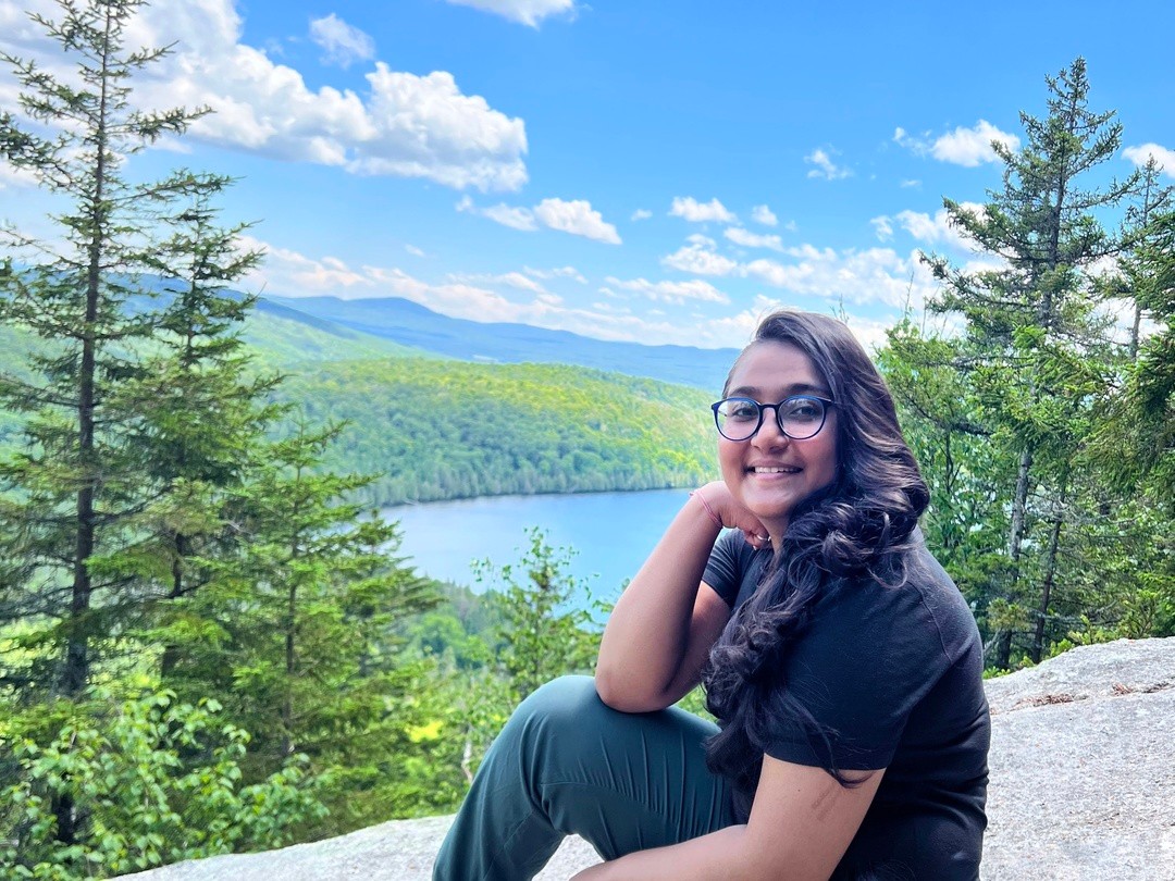 A young woman poses in front of a scenic river and autumn landscape.