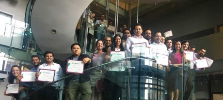 The second cohort of Lean Six Sigma group standing on a spiral staircase holding their certificates