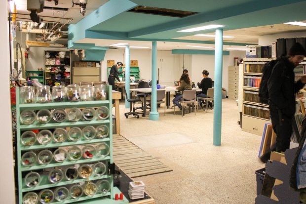 A photo of the Concordia University Centre for Creative Reuse showing different materials housed on shelves and tables as well as people browsing the materials and crafting at a table.
