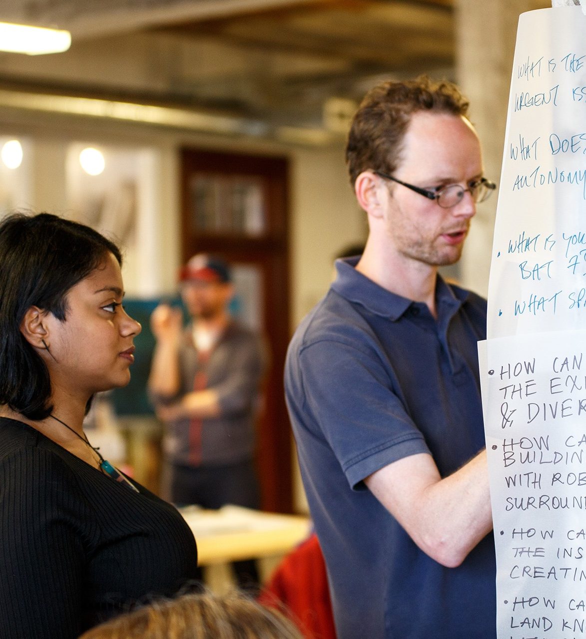 a woman and man writing on paper taped to the wall in a group setting