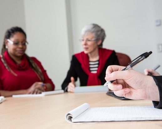 close-up of a hand poised to take notes during a group discussion