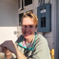 A person with short blonde hair smiles with the sun on their face