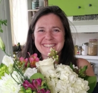 Woman with long dark hair smiles while holding a large bouquet of flowers in a kitchen setting. 