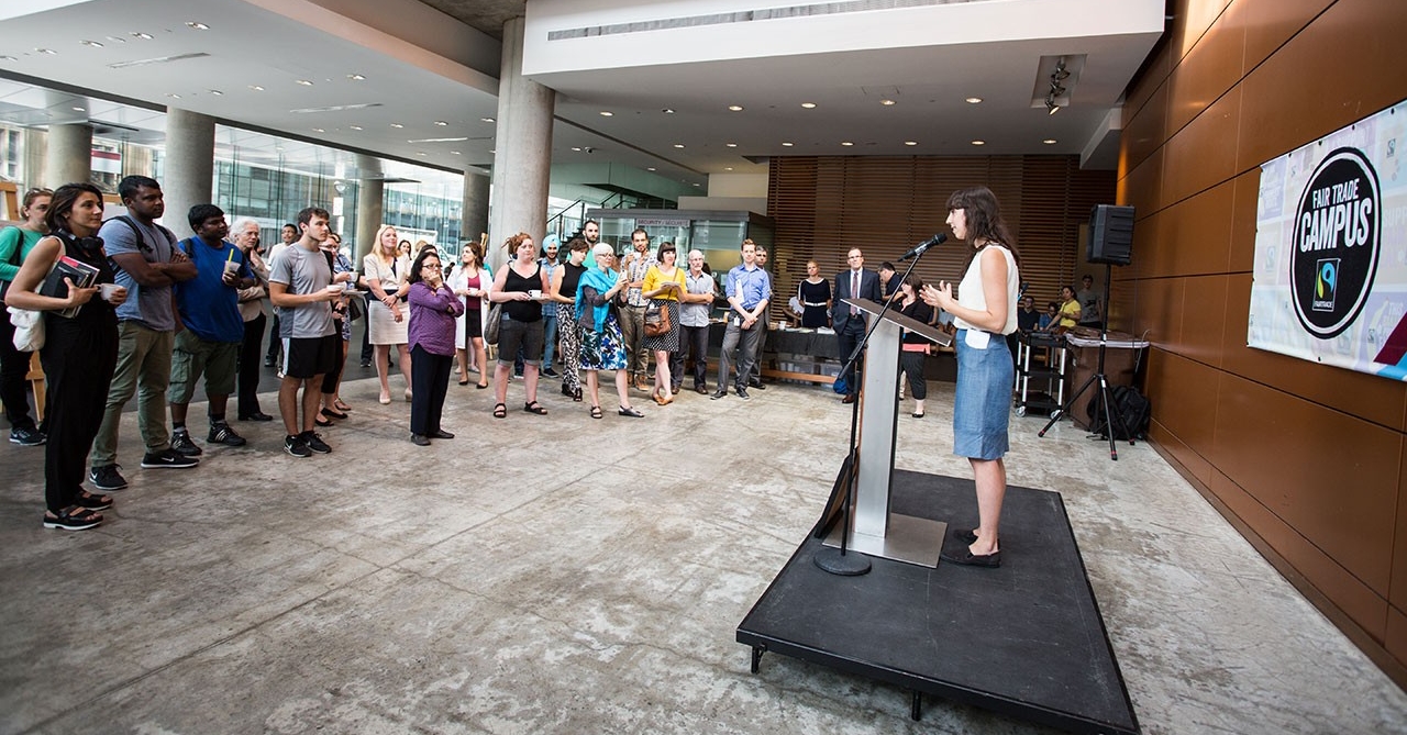 A person on a small podium speaking to a crowd about Concordia's faitrade campus status.