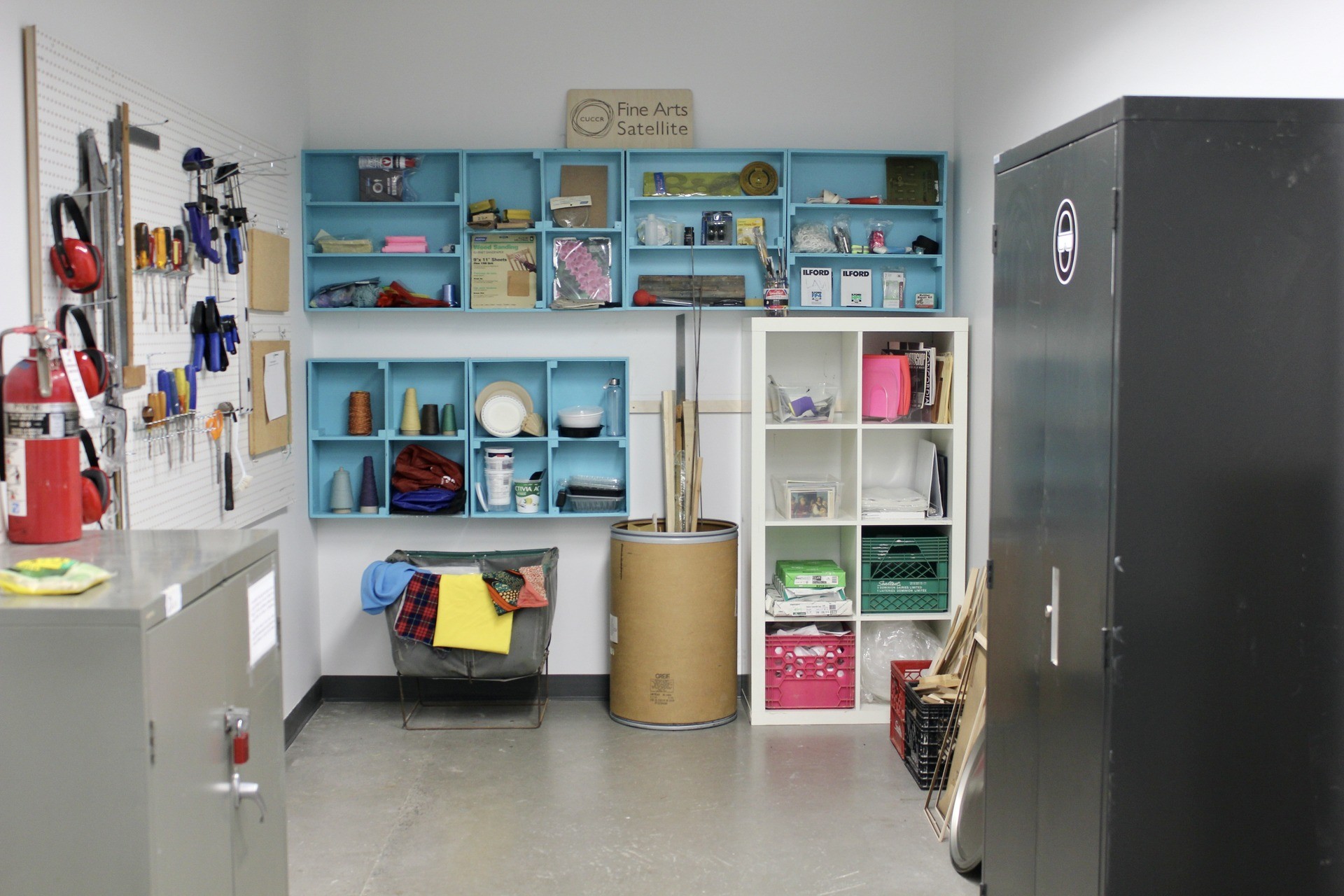 A small room with coloured shelves, cabinets, and other receptacles, all full of art supplies