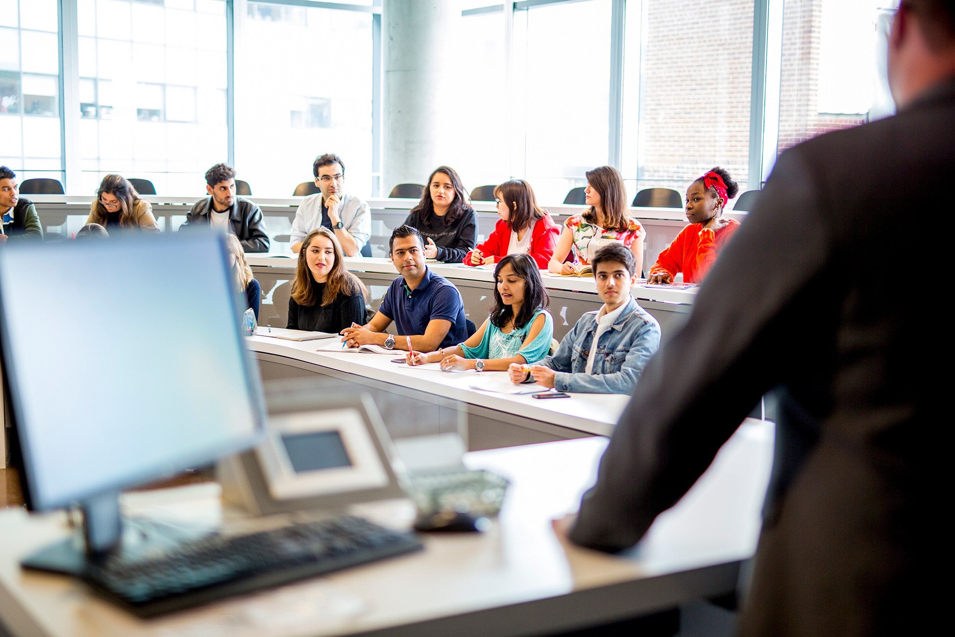 A class of seated students is photographed from behind the professor