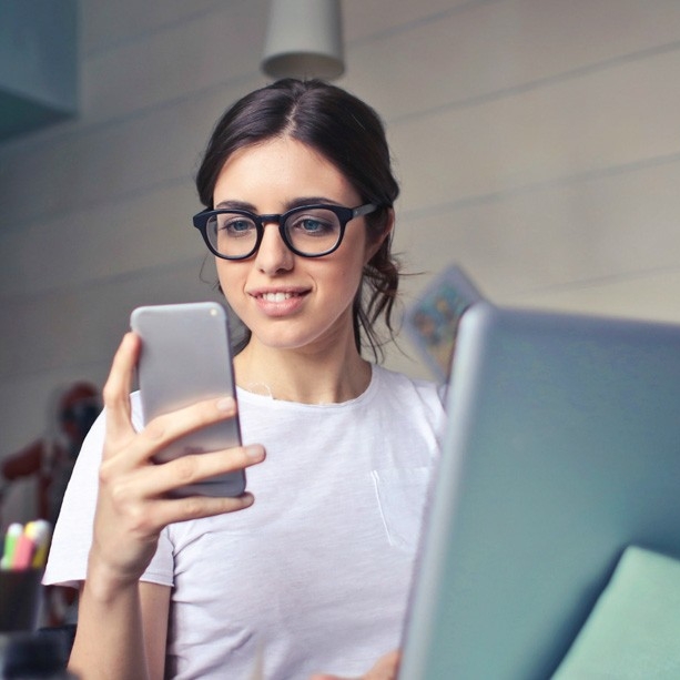 Woman at a computer looking at her mobile phone