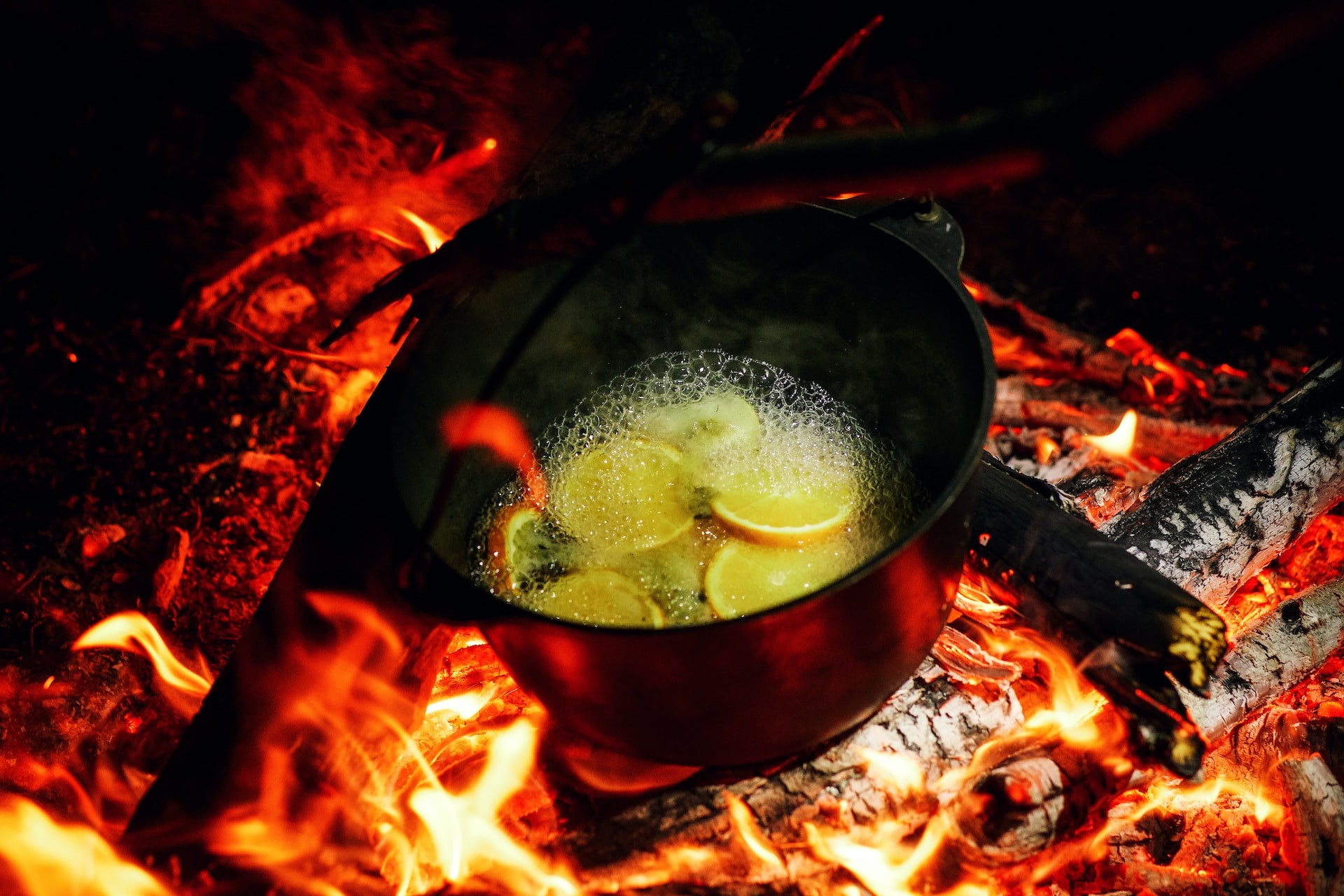 Sliced lemons boiling inside a cauldron over an open fire and red embers