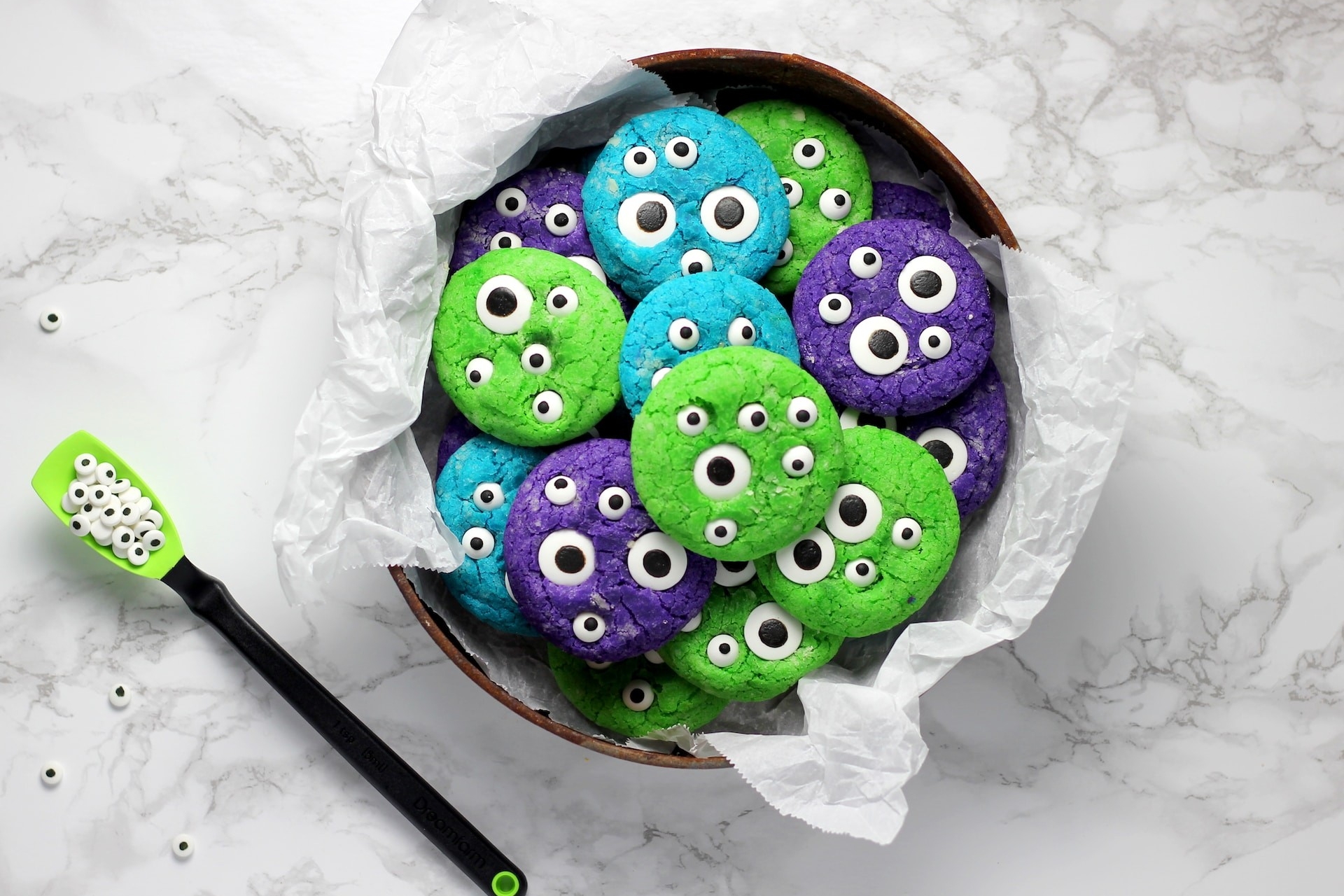 white tin of blue, purple and green cookies with black and white eyes