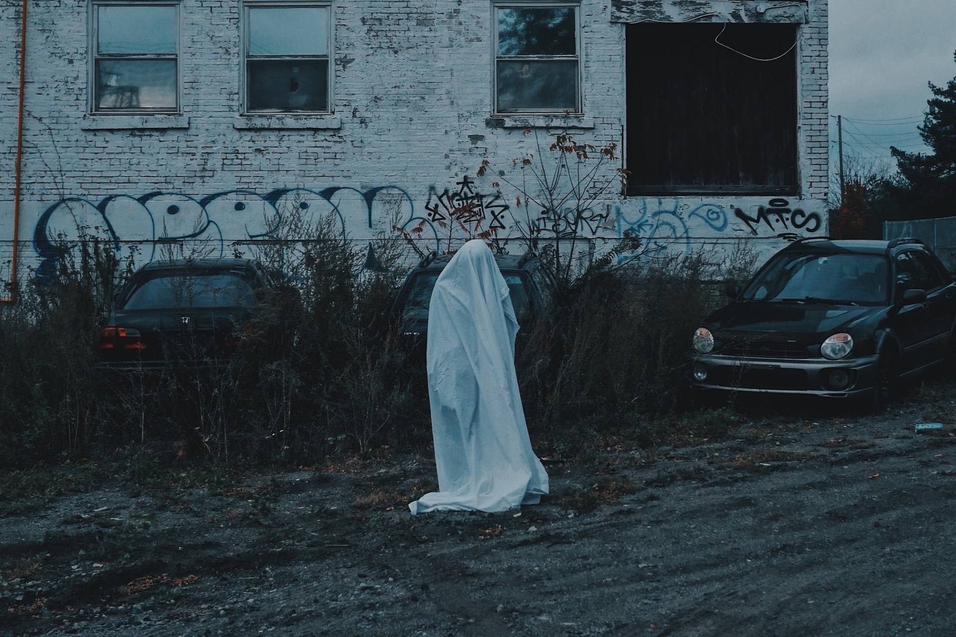 Ghost standing in front of white brick building that is covered in grafitti