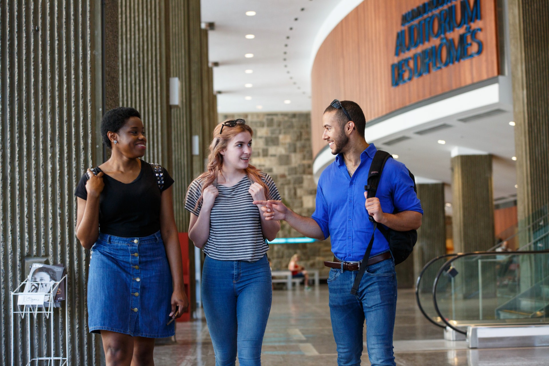 Three smiling students walking and talking in the Hall Building