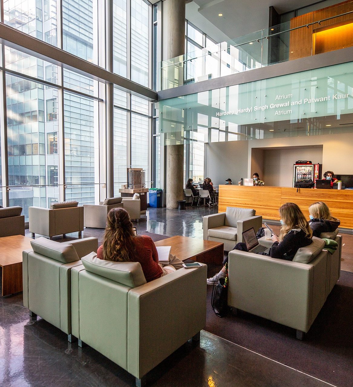 Students sit in sofa chairs in a large open space with large glass windows. Students sit in sofa chairs in a large open space with large glass windows.