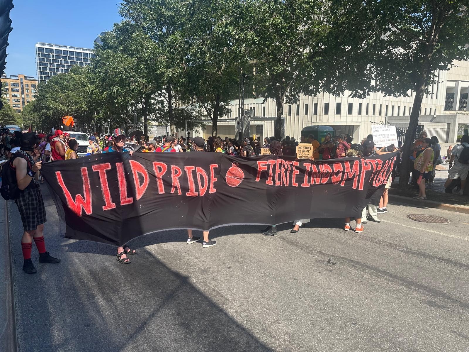 Photograph of a parade, with people holding a large black and red banner reading "Wild Pride"
