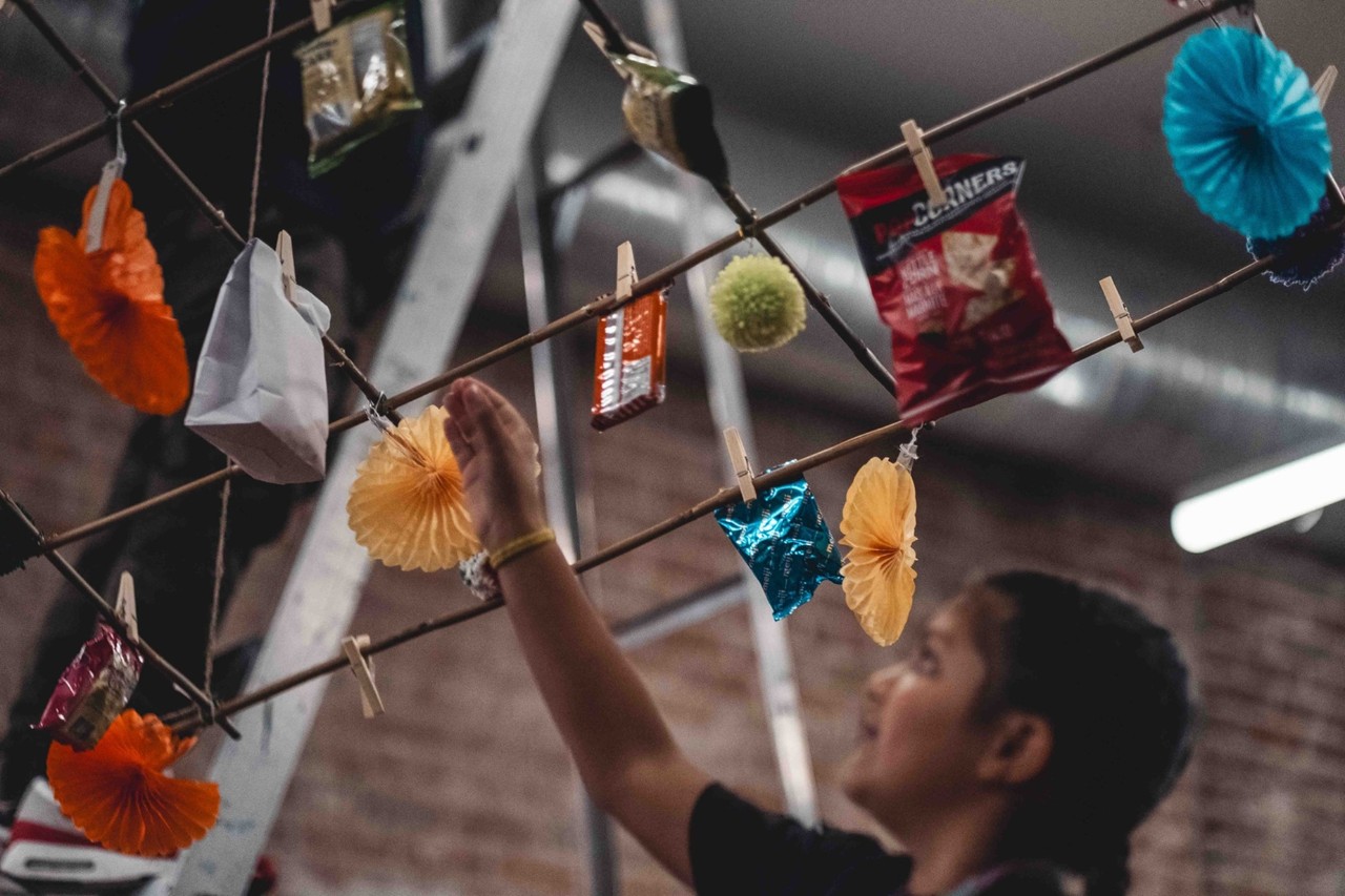 A smiling person putting items--snacks, fans, and bags of tea--on a trellis using clothes pins