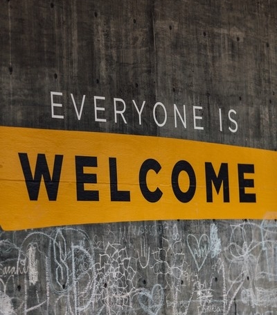 Un mur de ciment gris avec les mots «Tout le monde est bienvenu » inscrits.