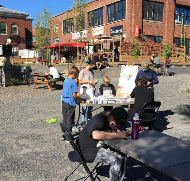 Une photographie de personnes pratiquant des activités artistiques à l'extérieur d'un bâtiment, dans un parking.