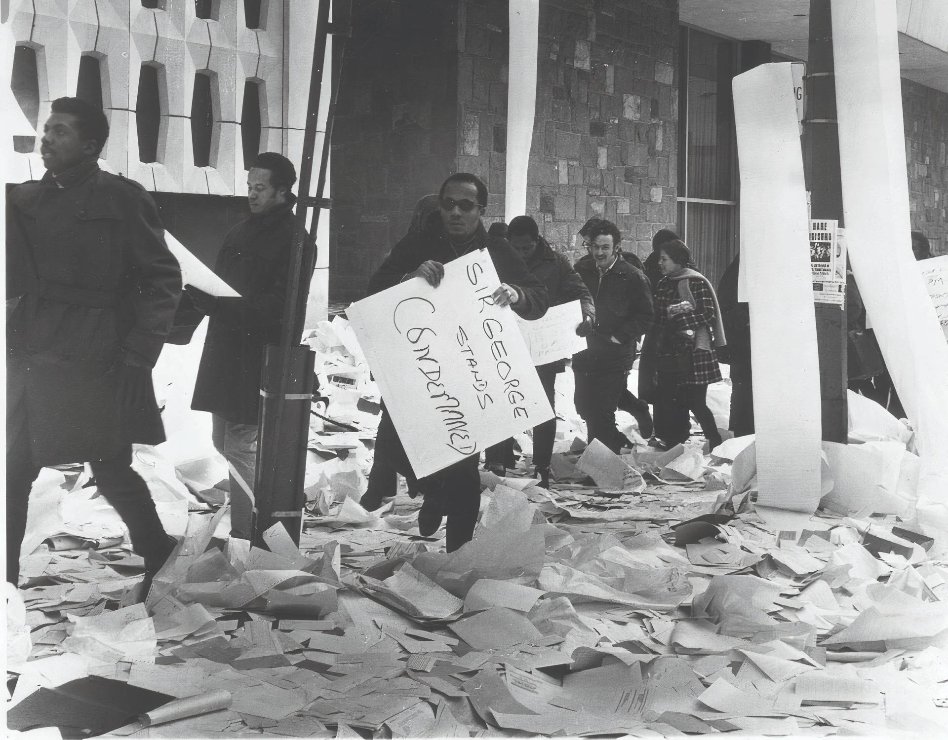 Protesters walk past the Hall Building, the ground and street posts littered with computer paper