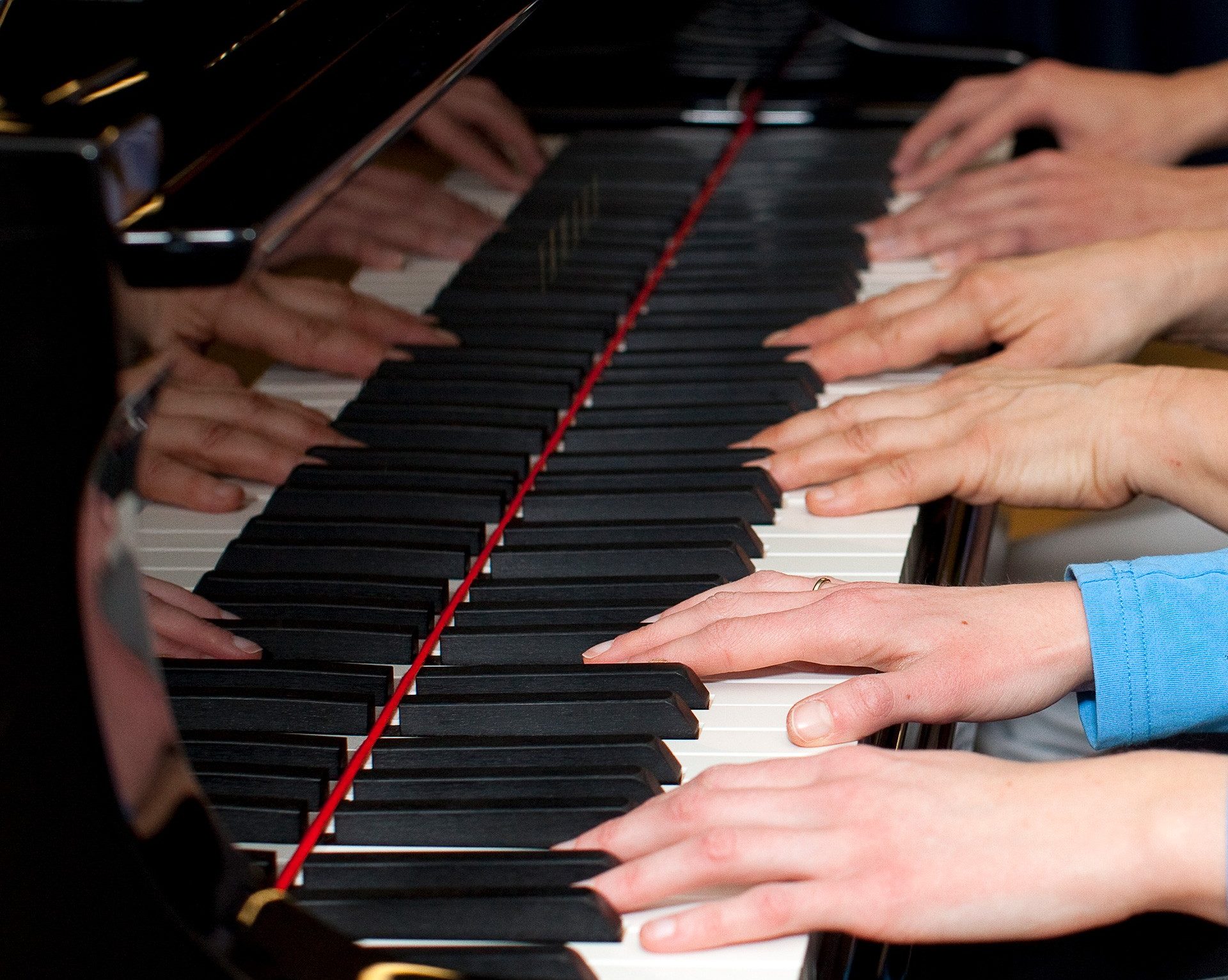 Close up of six hands on a piano keyboard.