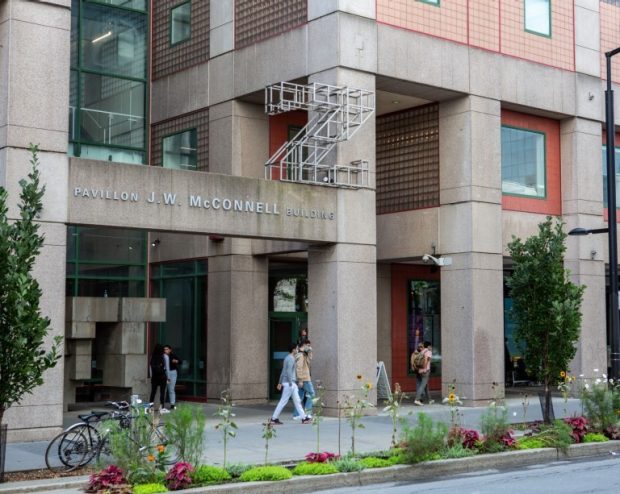 Entrée du pavillon J.-W.-McConnell de l’Université Concordia, avec des personnes marchant devant l’entrée et de la végétation le long du trottoir.