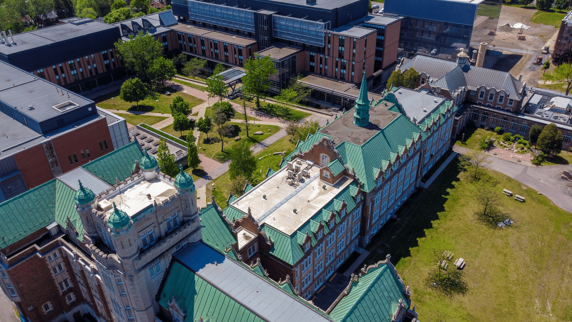 Vue aérienne d'un campus universitaire avec des bâtiments historiques dotés de toits verts, des structures modernes, des arbres et des espaces verts.
