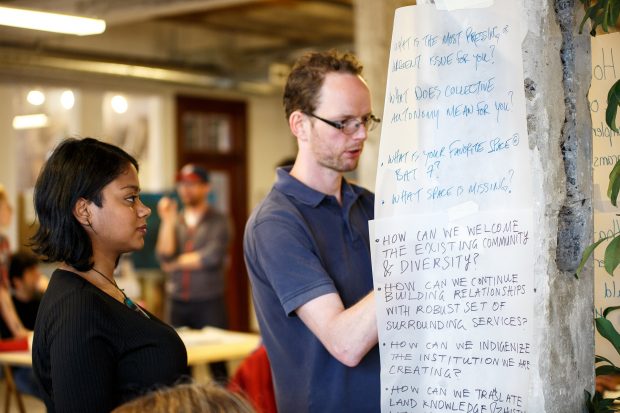 a woman and man writing on paper taped to the wall in a group setting