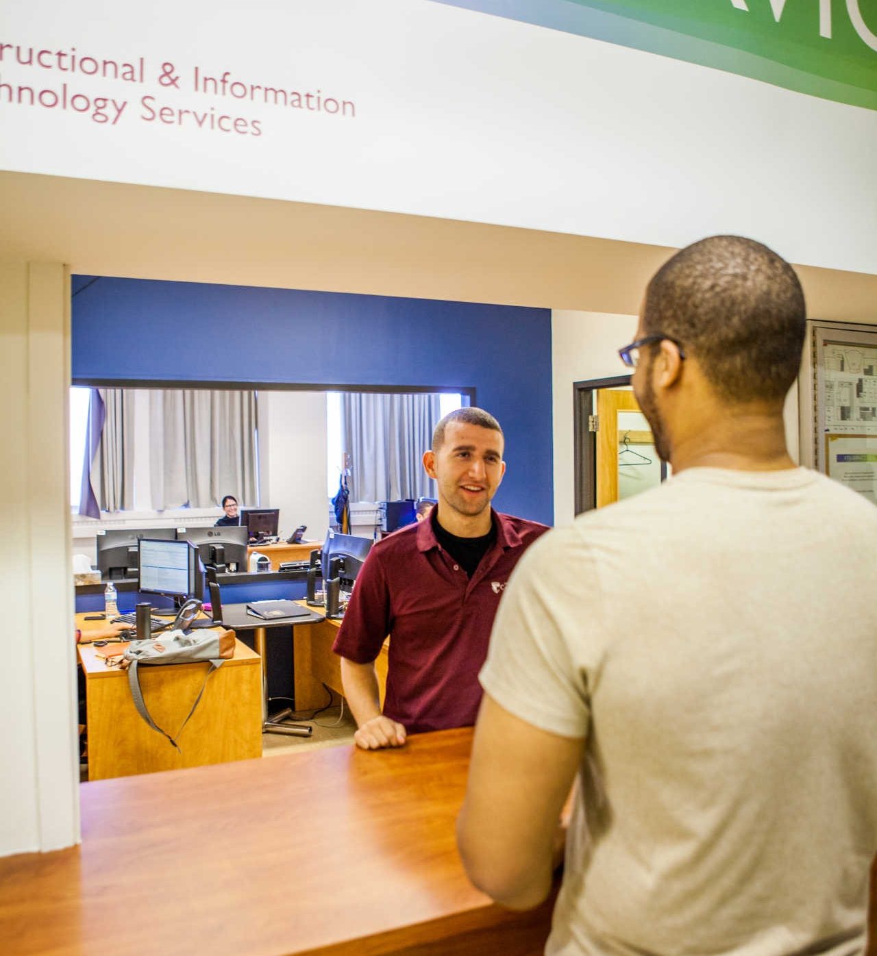 Un homme debout au comptoir du centre d’assistance du Service des technologies de l’information et de l’enseignement parle avec un étudiant.