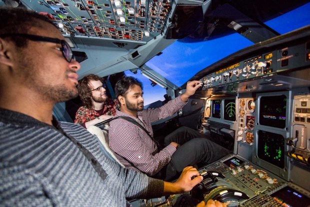 Three men in a flight simulator cockpit