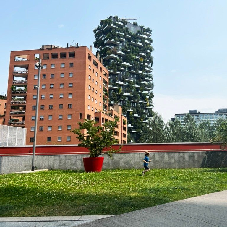 Futuristic urban setting showing a young child running across green grass.