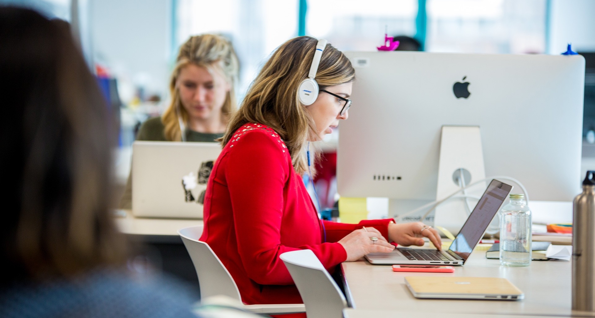 Mise à niveau du système de téléphonie de l’Université Une femme portant des écouteurs travaille à un bureau avec un ordinateur. Une autre femme se trouve à l'arrière-plan, utilisant également un ordinateur.