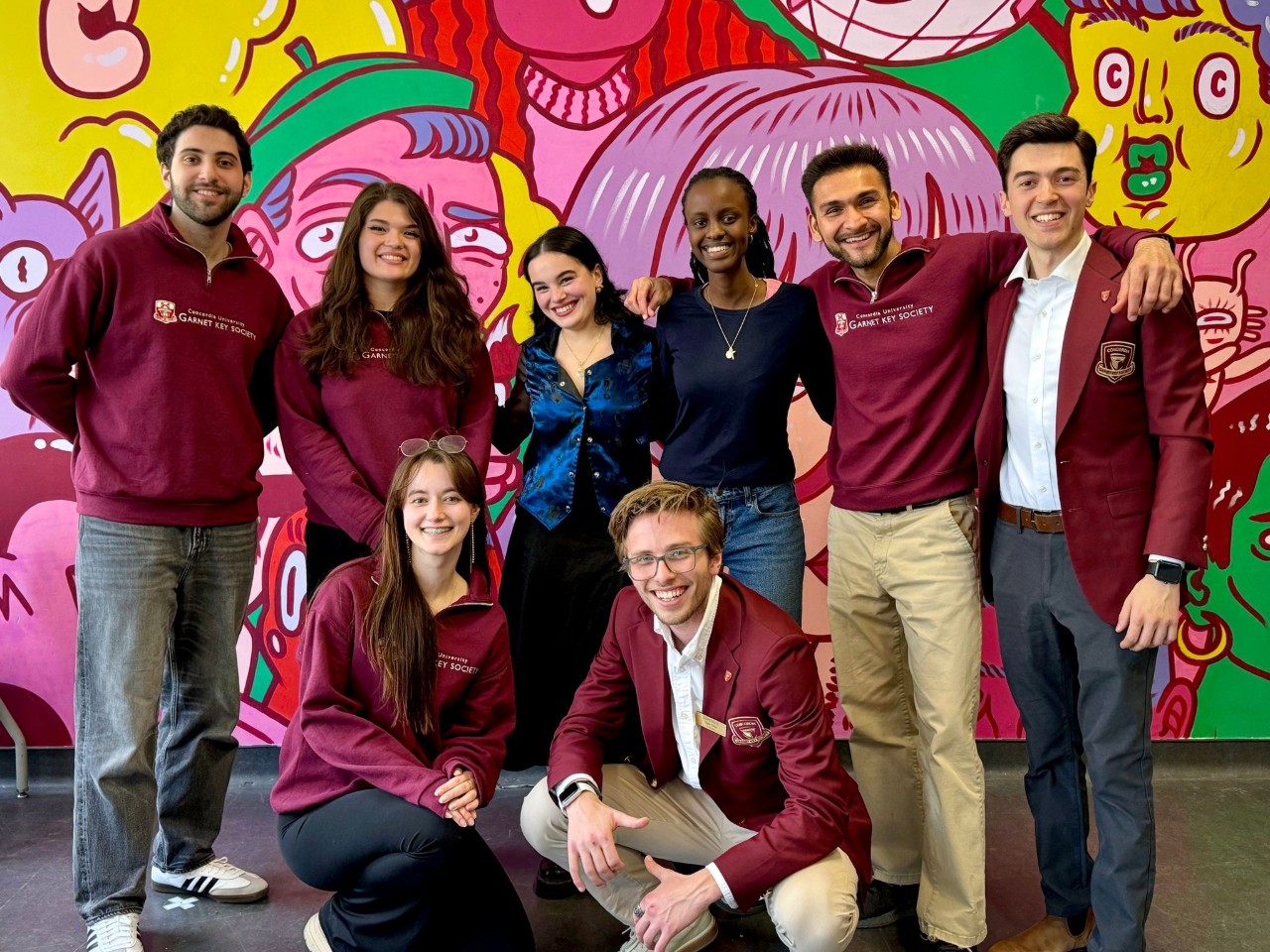 Group of students pose in front of a colourful mural