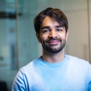 Un homme aux cheveux noirs courts et à la barbe est vu souriant