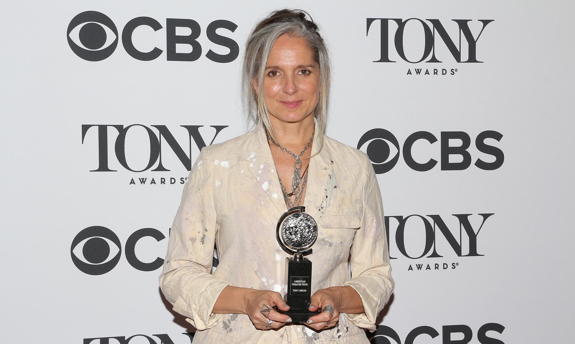 Christine tient son Tony Award et se tient devant un arrière-plan sur lequel figurent les logos de CBS et des Tony Awards.